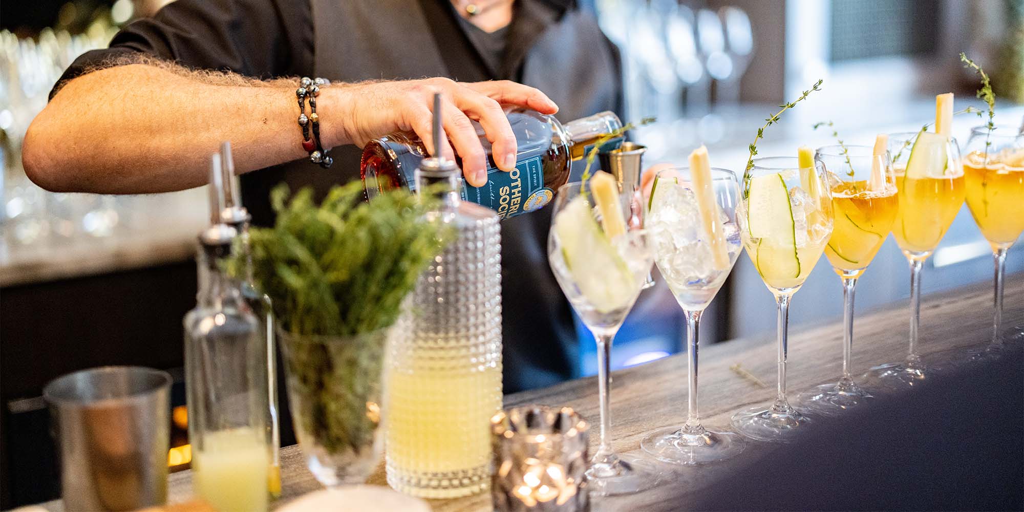 Mixologist pouring Otherland Society Wild Hare Dark Rum into a cocktail mixer behind a bar lined with Hurricane Thyme cocktails