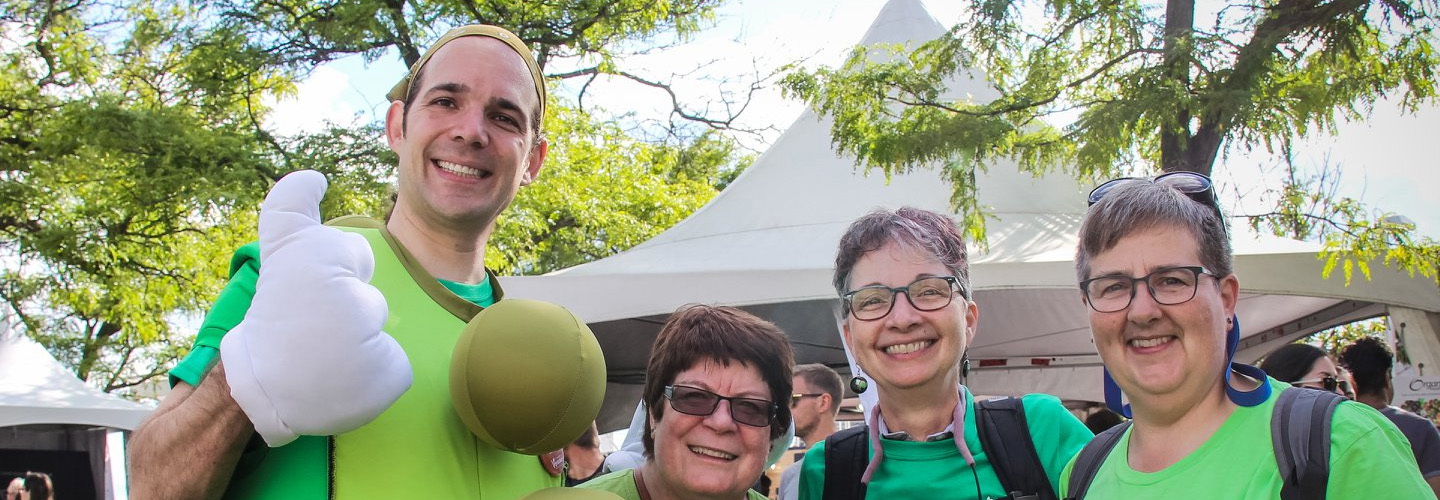 A group of four people enjoy their time at Veg Fest, wearing bright green TVA tops and a pea pod costume.