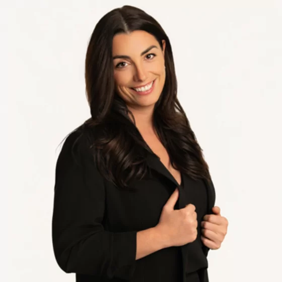Smiling woman with long dark hair wearing a black jacket against a plain white background.