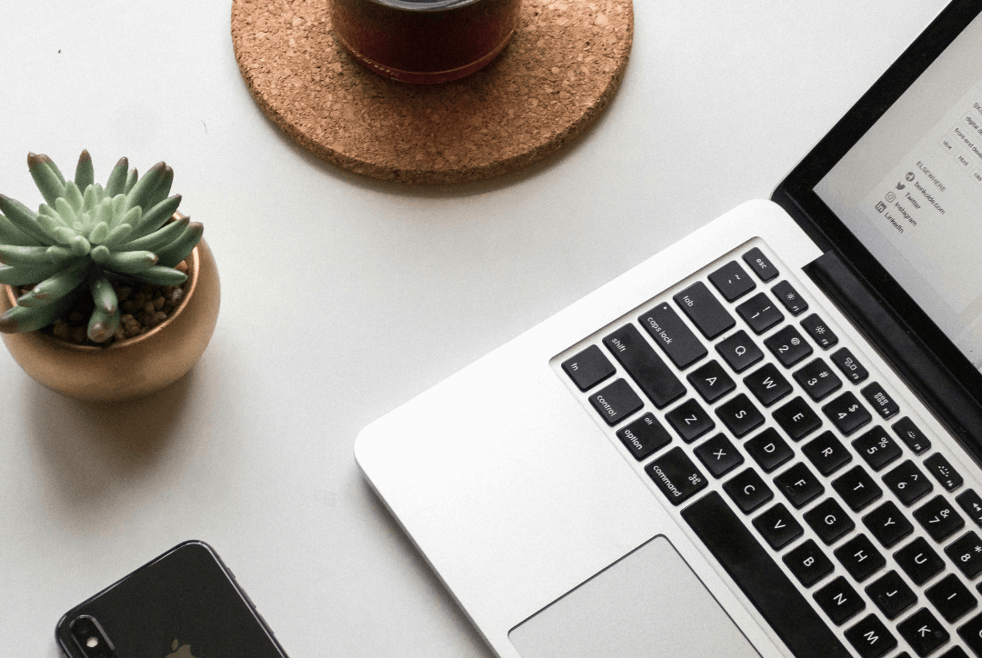 Real estate agent using a laptop with a smartphone and coffee to create marketing content with the help of an AI content generator