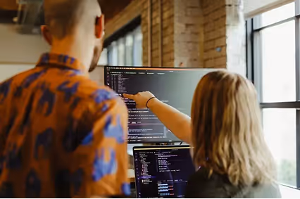 Two professionals collaborate on software development, reviewing code and engaging in discussion.