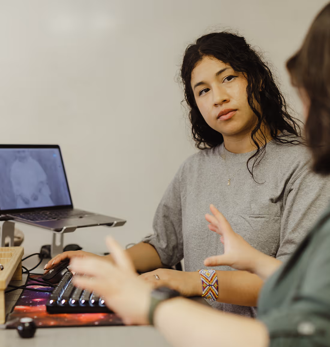 Two Atoms engaged in a conversation while working on a computer, one attentively listening and the other gesturing.