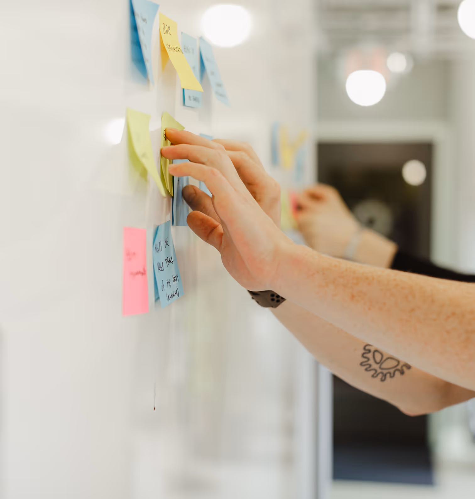 Two Atoms organizing colorful sticky notes on a whiteboard in an office.