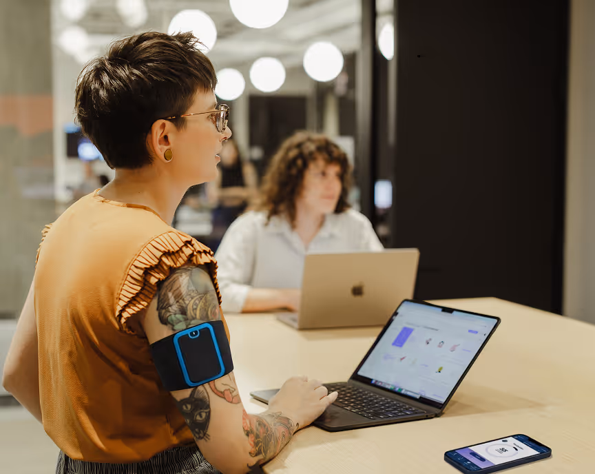 Person with tattoos using a laptop at a workspace, showcasing a modern healthcare tech environment.