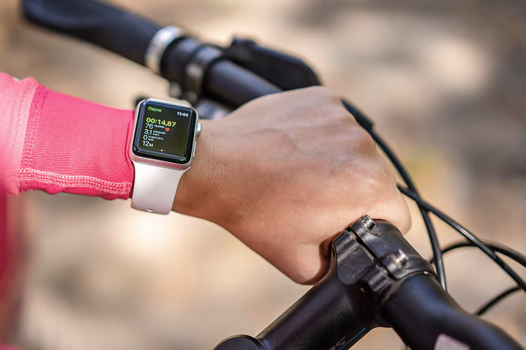 Close-up of a person's hand gripping bike handlebar while wearing a smartwatch displaying exercise stats.