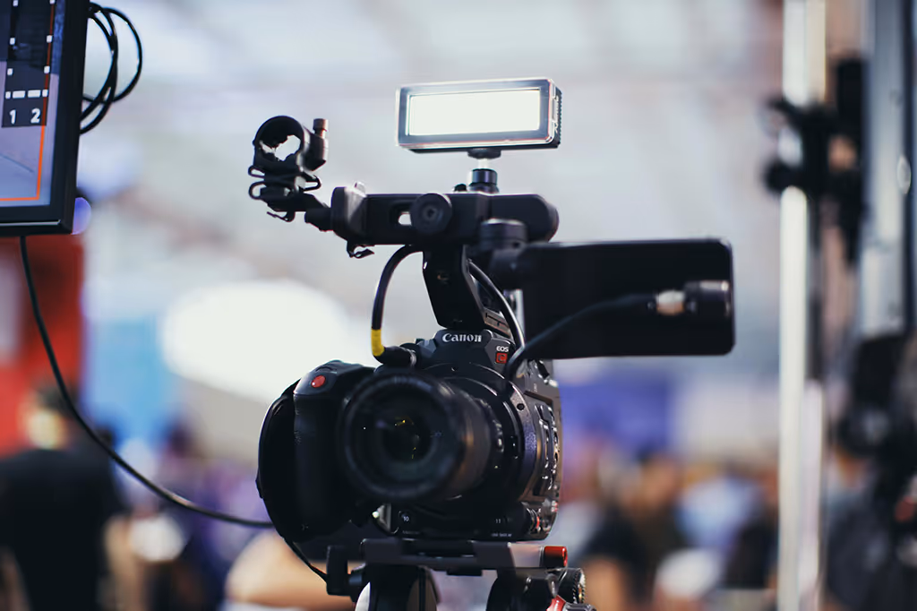 Professional Canon EOS video camera with attached light and microphone on a tripod in a blurred indoor setting.