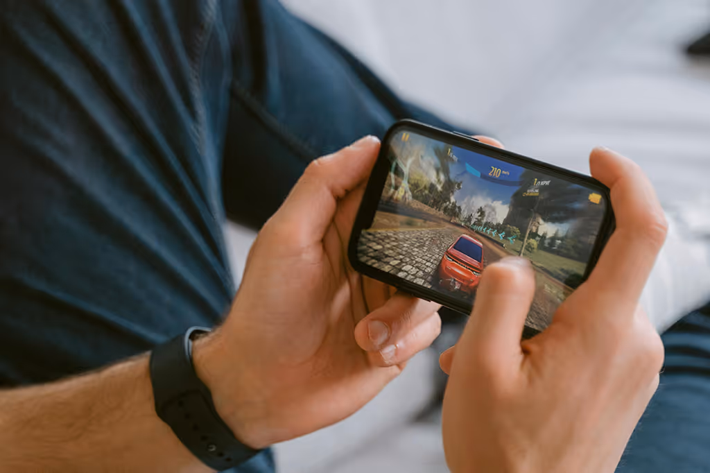Person holding a smartphone playing a racing game with a red car on the screen.