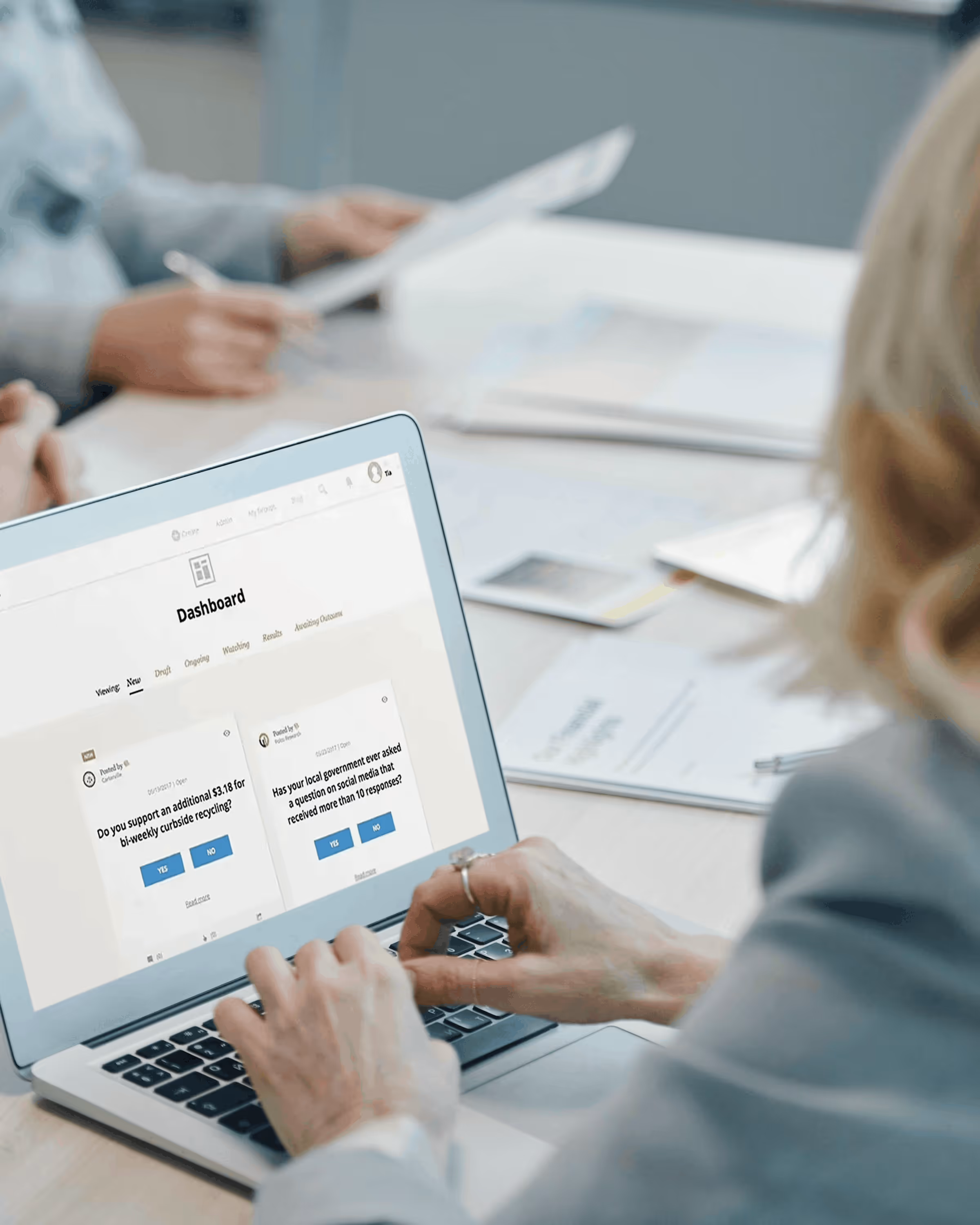 Person typing on a laptop showing a dashboard with survey questions about local government and recycling support.