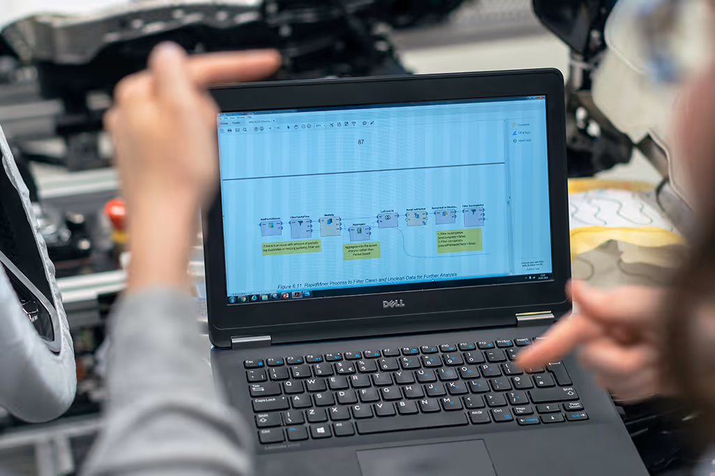 Two people pointing at a Dell laptop screen displaying a data analysis workflow diagram.