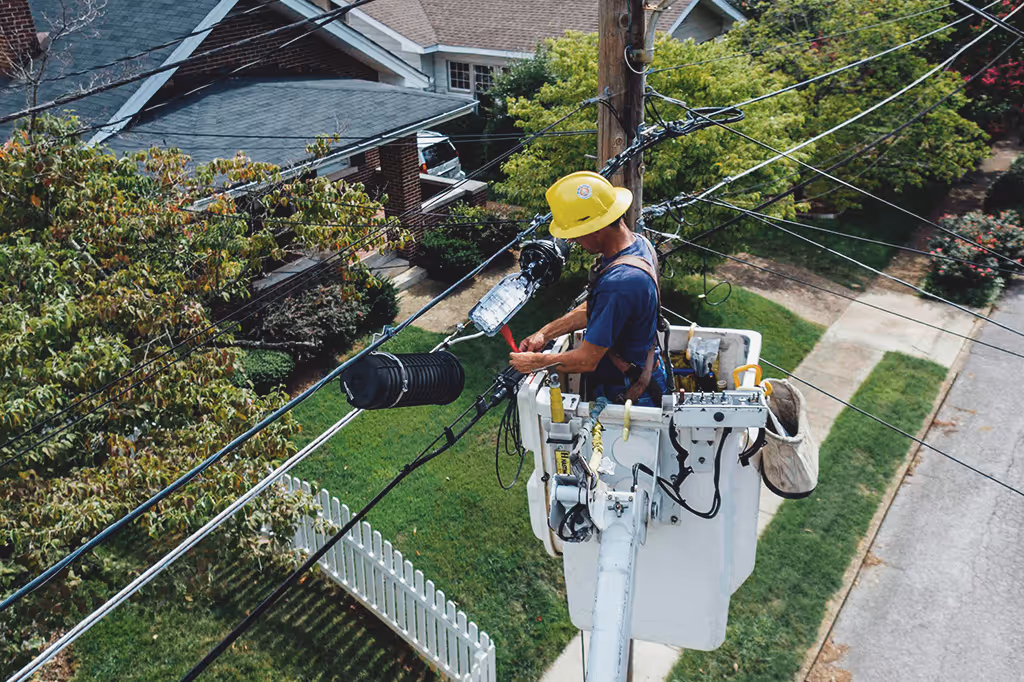 Utility worker in a bucket lift repairing or maintaining overhead power lines near residential houses.