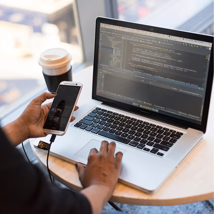 Atomic Object team member coding on a laptop while using a smartphone, enhancing web app development.