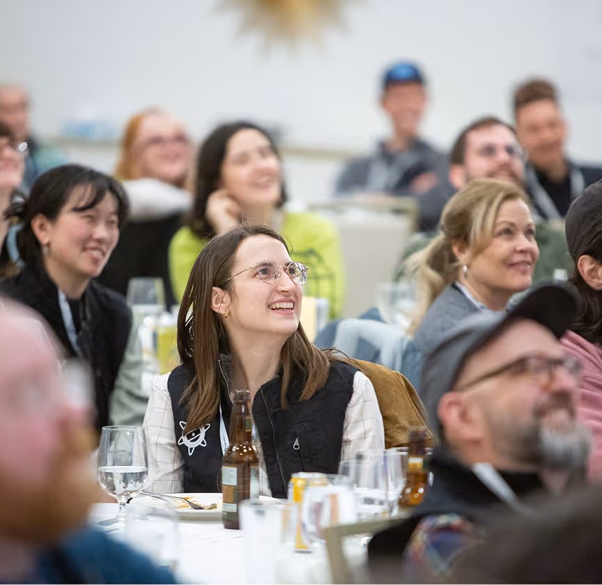 Attendees at a conference engage, smiling and sharing laughs during a presentation in a lively setting.