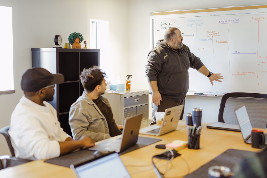 A team meeting in an Atomic Object office, discussing project strategies using a whiteboard.