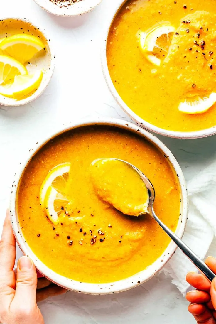 This may contain: two bowls of soup with spoons in them and lemon slices on the table next to it