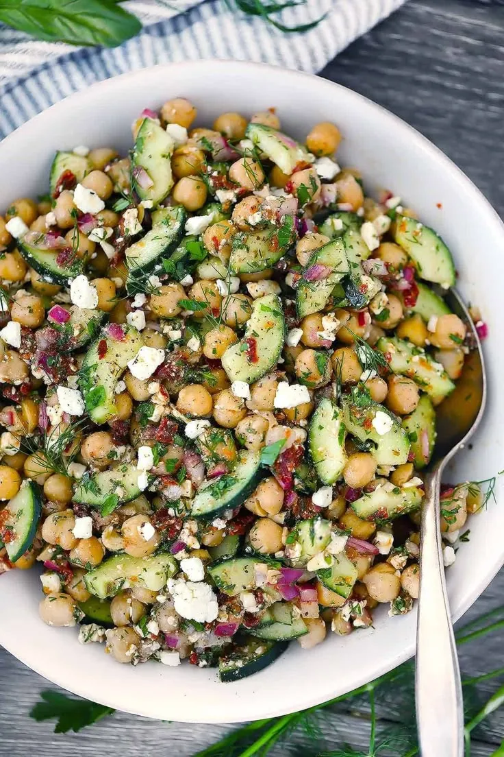 This may contain: a white bowl filled with cucumber, chickpeas and feta cheese