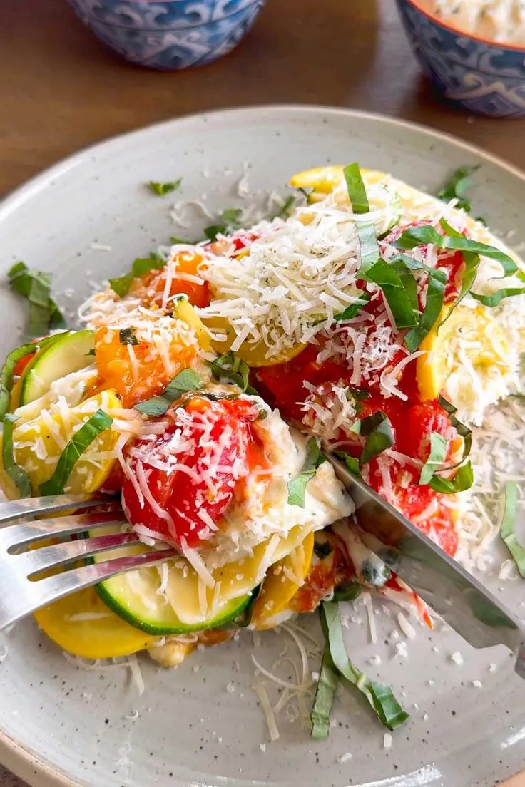 This may contain: a white plate topped with lots of veggies covered in sauce and parmesan cheese