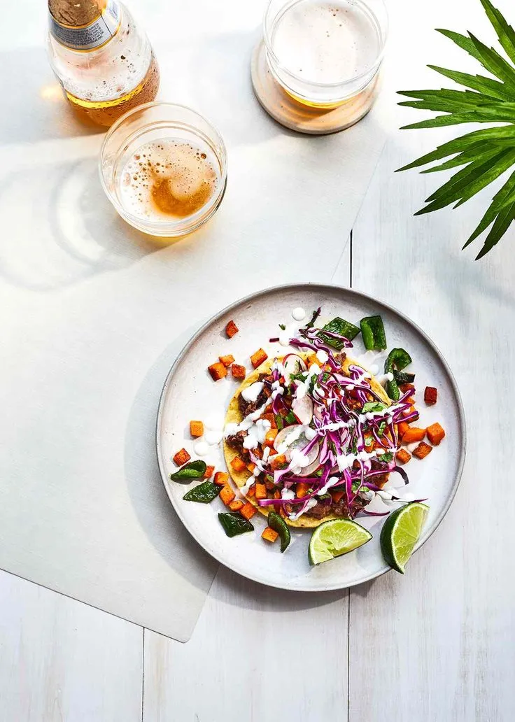 This may contain: a white plate topped with salad next to two glasses of beer and a potted plant