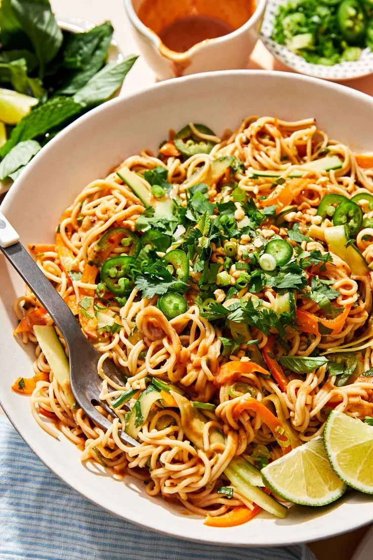 This may contain: a white bowl filled with noodles, carrots and cilantro on top of a table