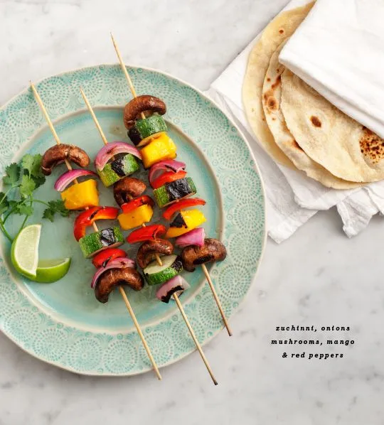 This may contain: several skewers of meat and vegetables on a blue plate next to tortillas