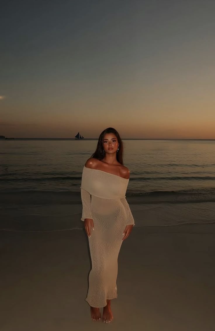 This may contain: a woman standing on top of a sandy beach next to the ocean at sunset or dawn