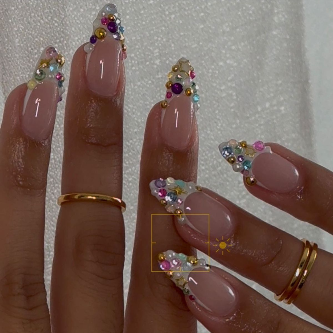 Pink nails with multi-colored gems on a white french tip. .