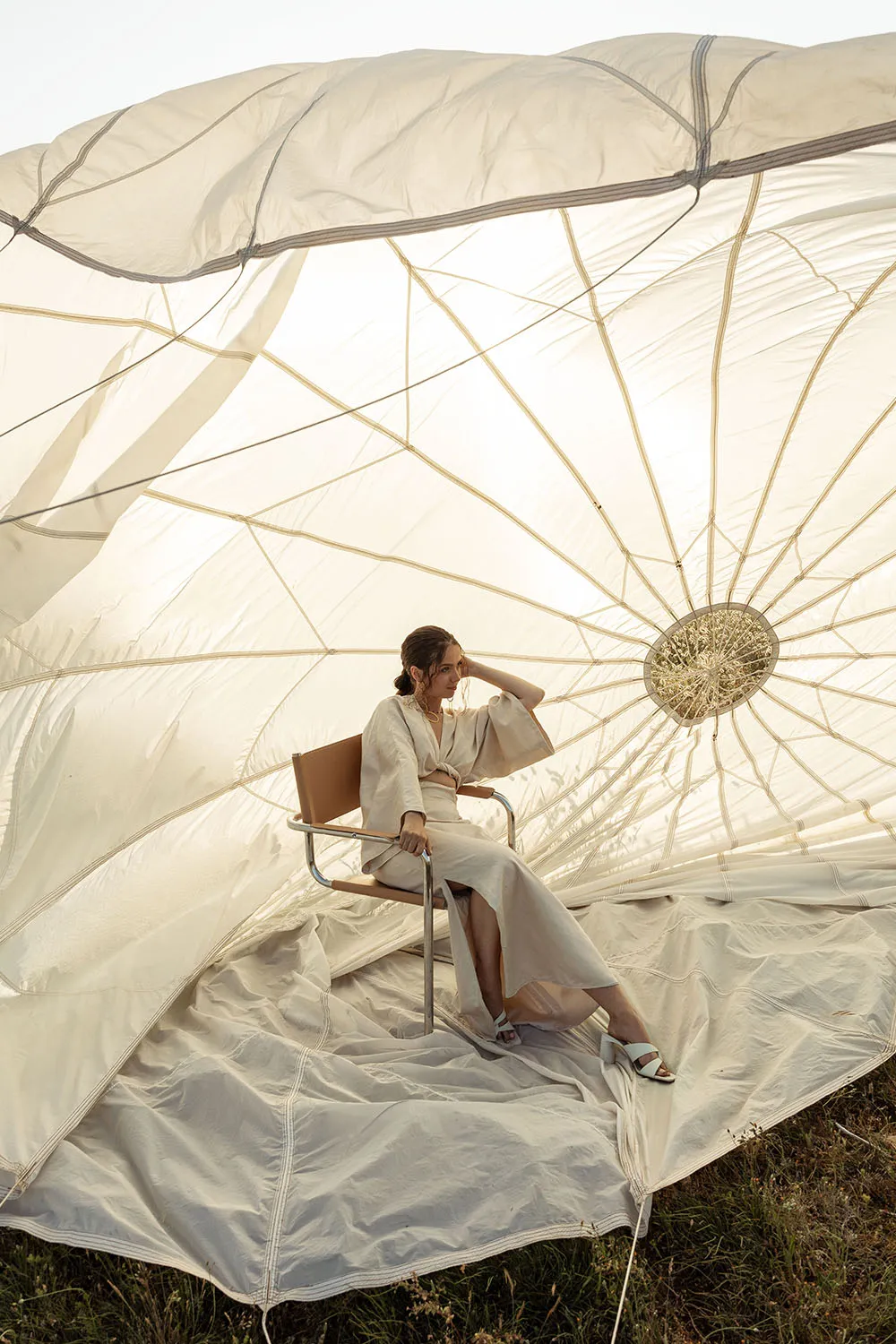 Photo éditorial mode, modèle assise sur une chaise design au centre d'un parachute blanc ouvert.