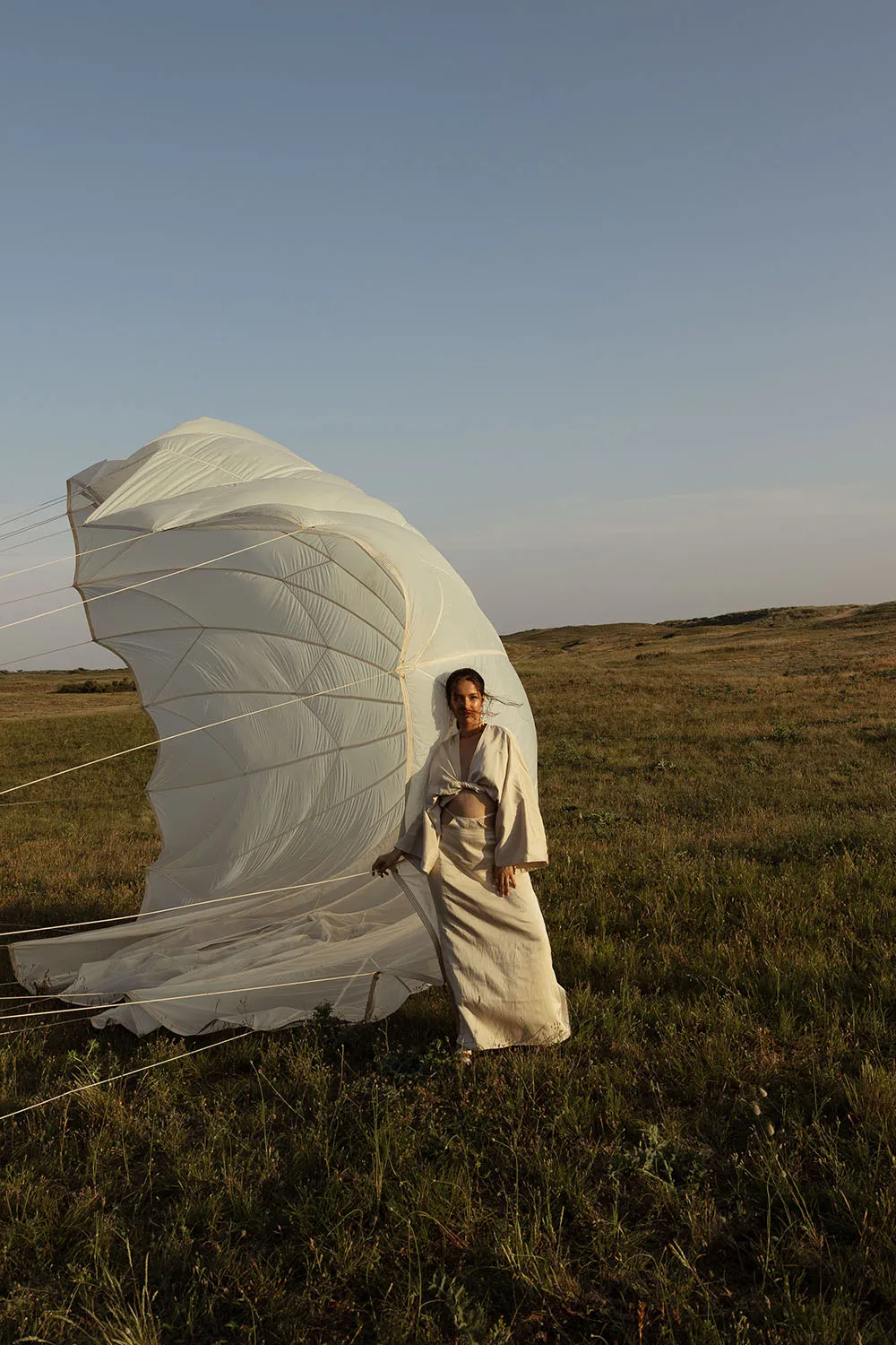Photo éditorial mode, mannequin avec un parachute blanc ouvert dans des dunes sauvages.