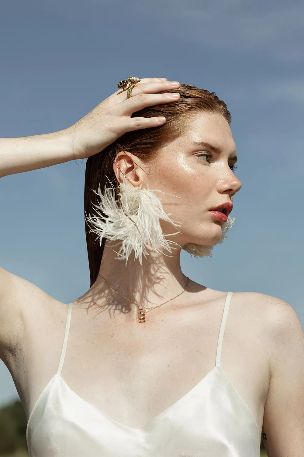 Photo éditorial portrait rapproché, modèle de profil avec une main sur la tête, fond minimaliste de ciel bleu.