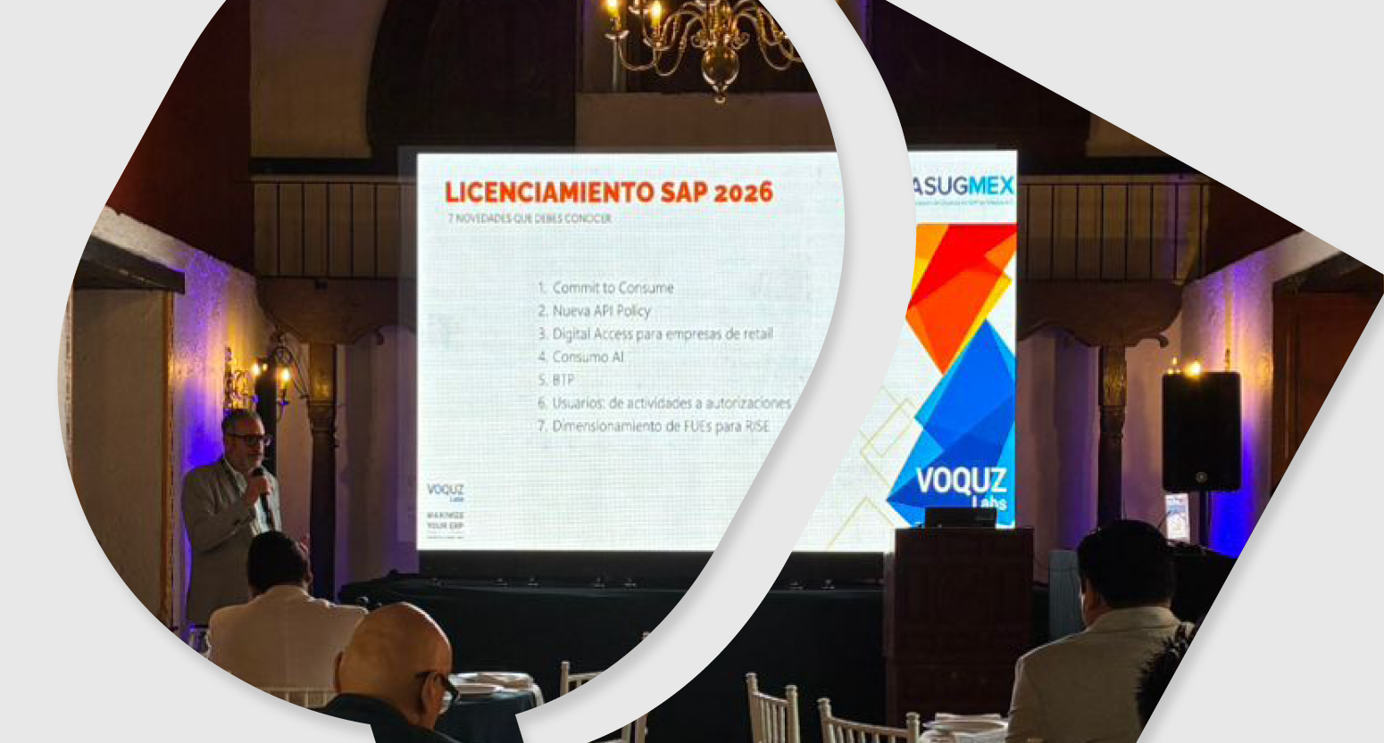 Man standing and speaking in front of a projected presentation slide titled 'LICENCIAMIENTO SAP 2026' with seated audience members in a dimly lit room
