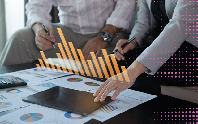 Two people discuss financial charts on a table, with a digital orange bar graph overlaying the scene, conveying a tone of collaboration and analysis.