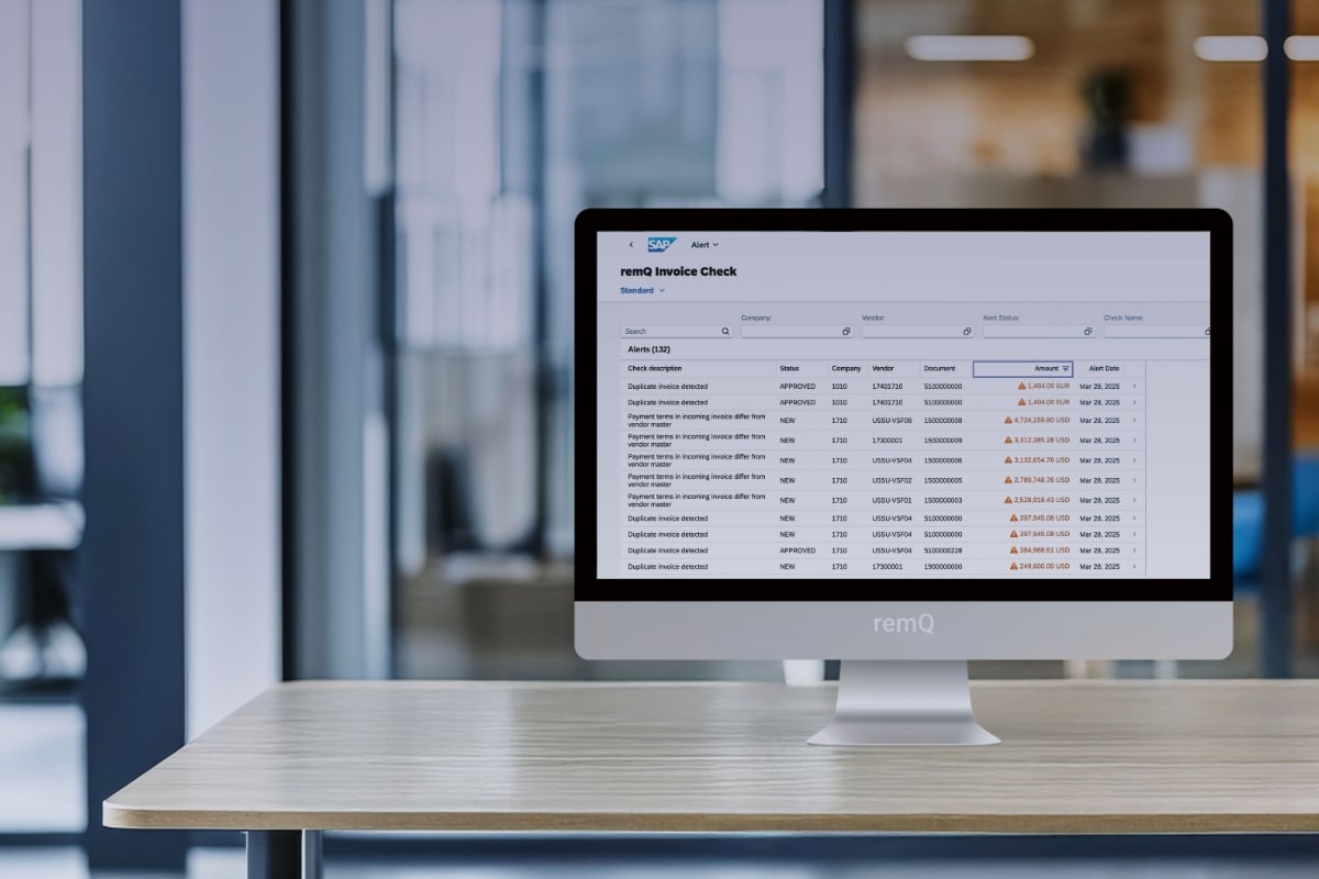 A computer monitor on a desk displays an invoice checklist with several rows, warnings and dates in an office setting.