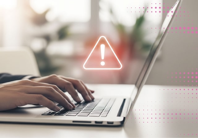 Close-up of hands typing on a laptop with a warning sign.