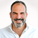 Smiling middle-aged man with short gray and black hair and a beard wearing a white shirt.