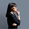 Woman with glasses in black outfit standing in profile with hand on chin, thinking.