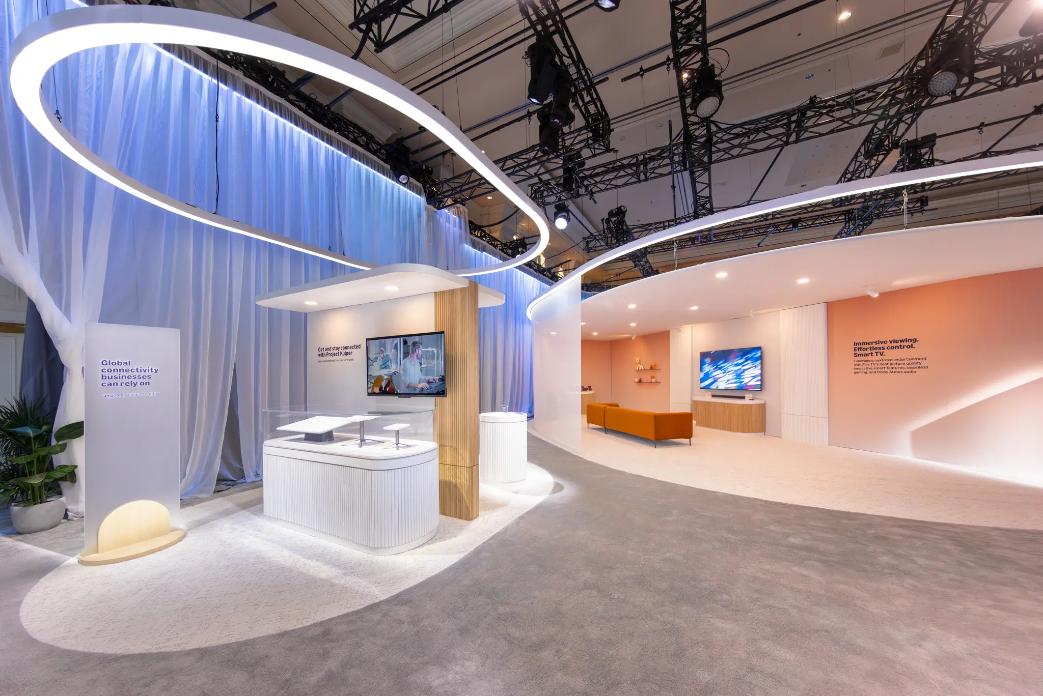 A sleek exhibition booth with modern design elements. Features include curved lighting, digital screens, and a cozy lounge area. The atmosphere is tech-focused and inviting.