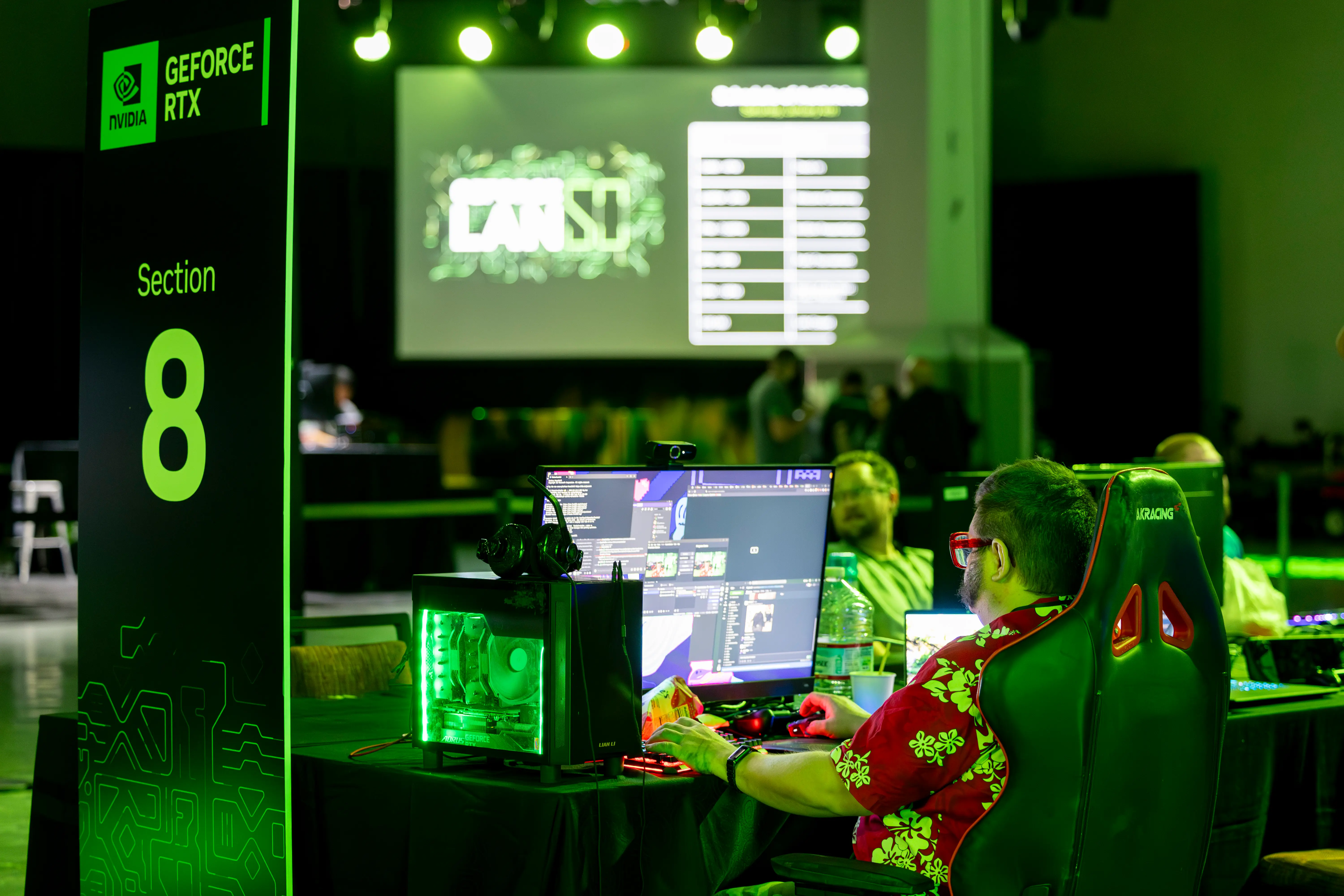 Person in a floral shirt at a gaming event sits at a computer in Section 8, with neon green lighting and an NVIDIA GeForce RTX sign nearby.