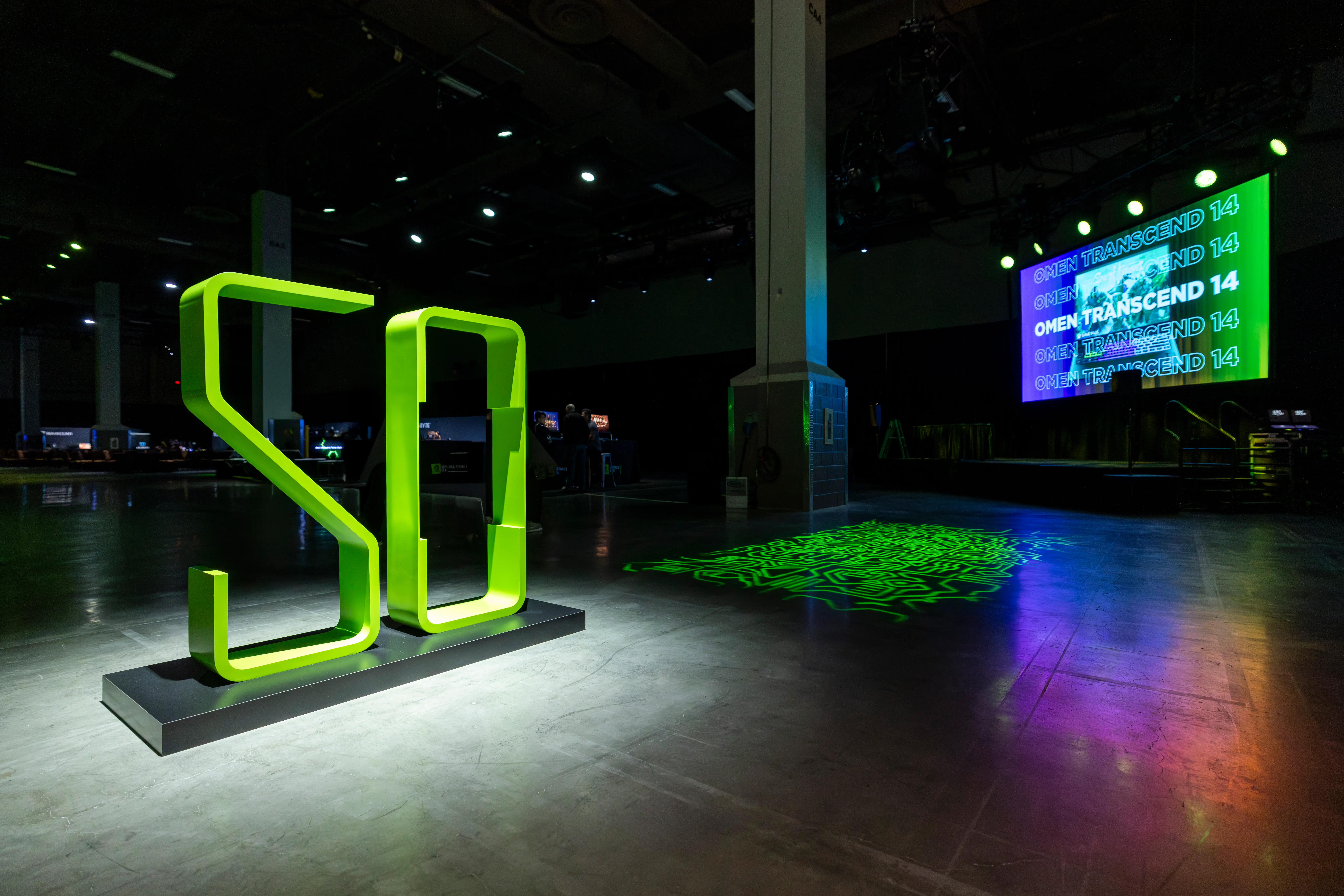 Dark event space with large, glowing green "50" sculpture in the foreground. A screen in the background displays "OMEN TRANSCEND 14" in vibrant colors.