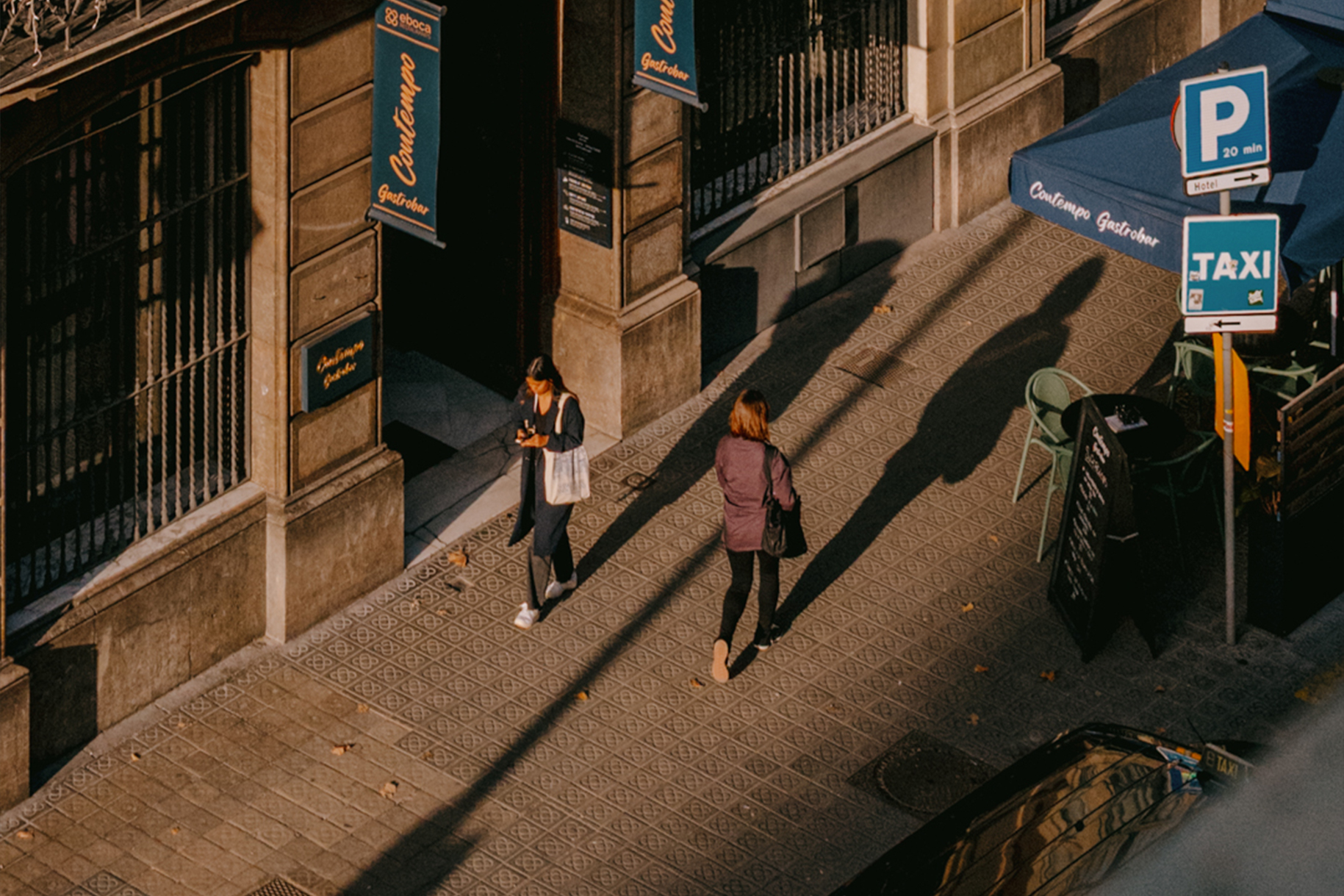 Late afternoon shadows on classic Eixample architecture in Barcelona, with pedestrians on tiled sidewalk