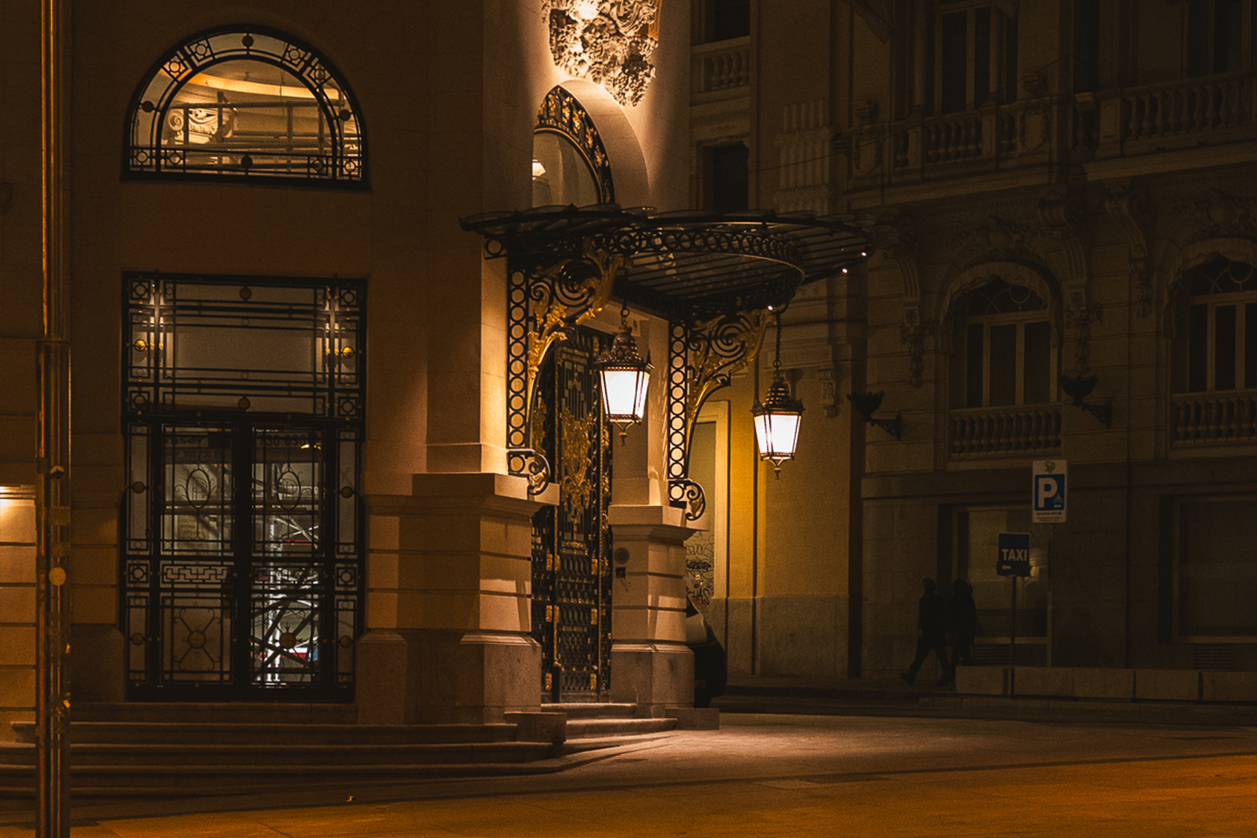 The ornate iron canopy and glowing lanterns at the entrance of The Westin Palace hotel in Madrid, taken by Jasmine Tam — reflecting grand but depersonalized luxury in upscale hospitality design.
