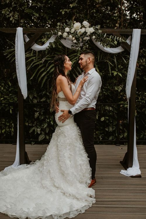 Couple kissing between arbour with white and green flowers. Woman wearing white wedding dress
