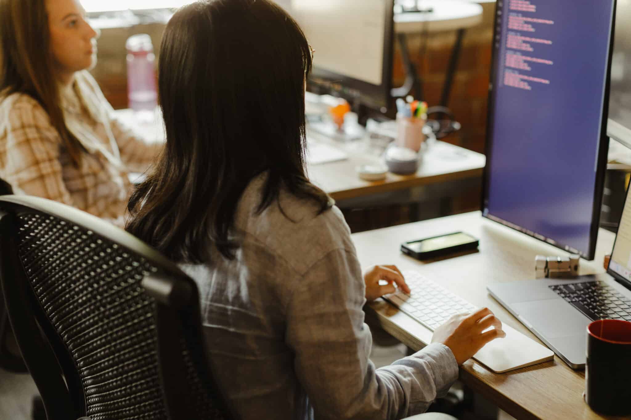 Developer Meghan Harris and a co-worker look at code on a monitor together. Post title: How My Software Development Team Upgraded Expo in a Monorepo