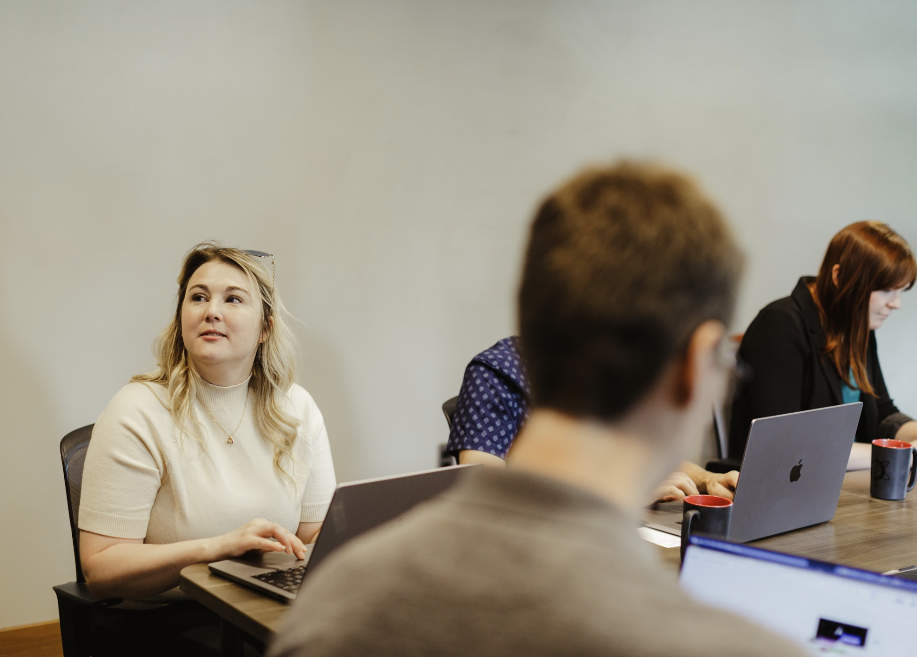 Two women sitting in front of a Dell computer monitor in an office, one explaining something while the other listens attentively.