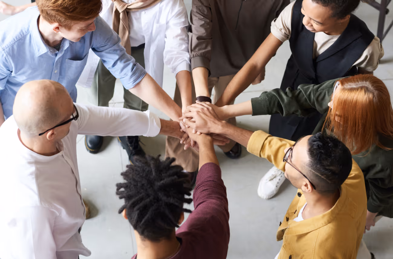 team of people putting their hands into the middle of a circle for a cheer