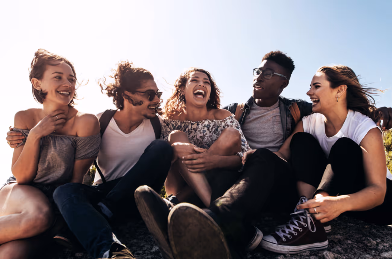 Group of young friends sitting in the sun smiling and laughing together