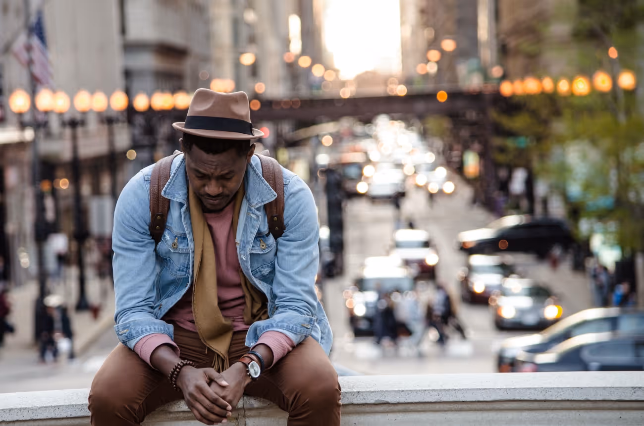 Man sitting on traffic barrier looking stressed and staring pensively at the floor 