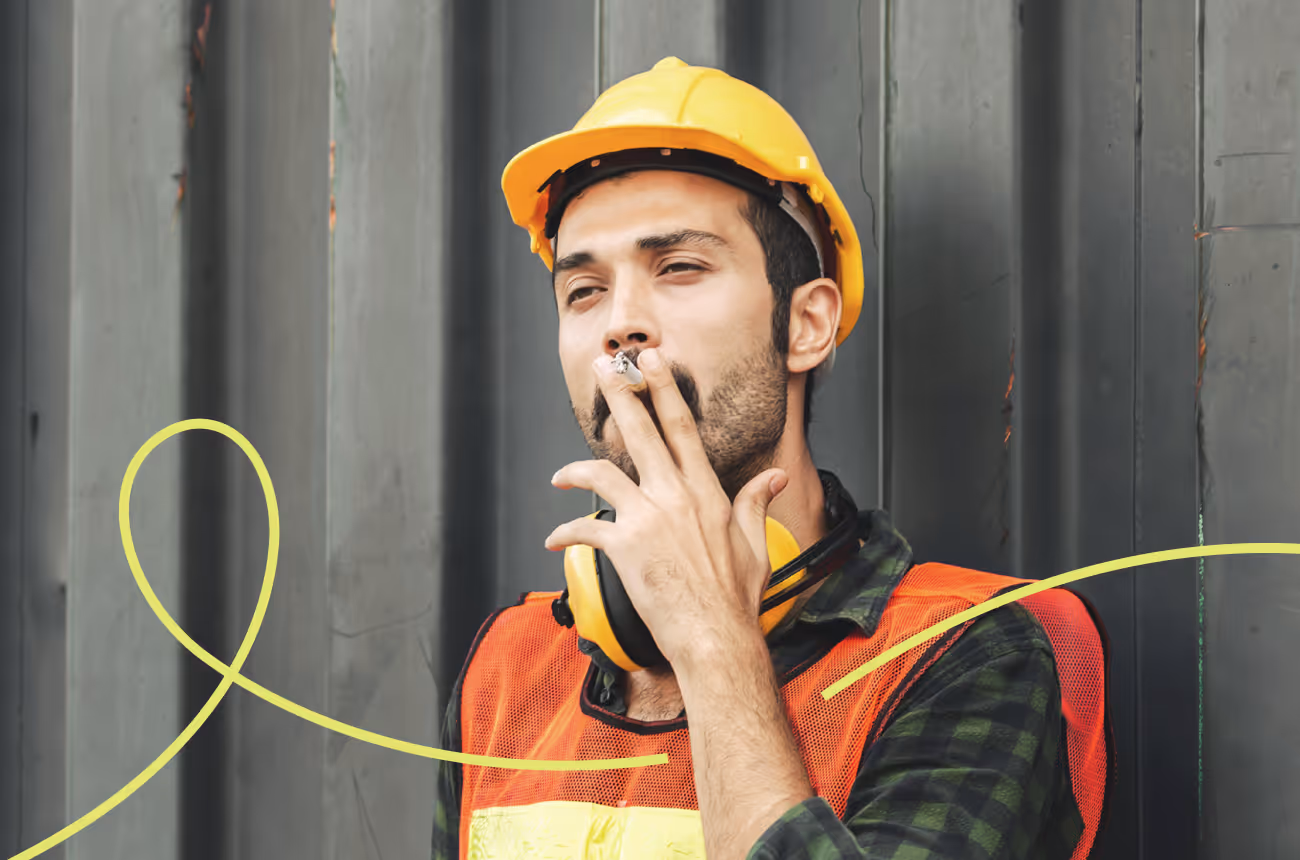 Male construction worker standing against wall smoking a cigarette