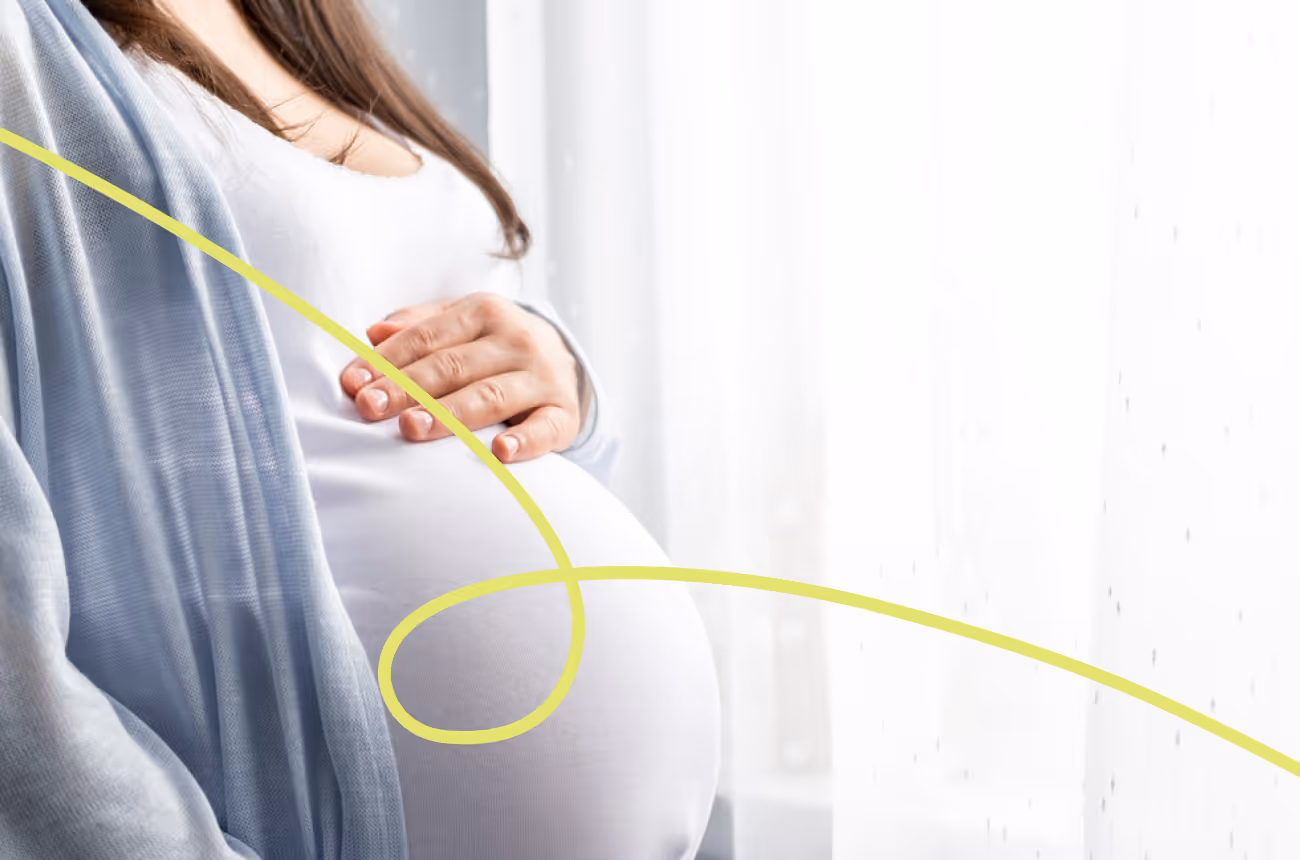 Pregnant person holding stomach and looking out their window