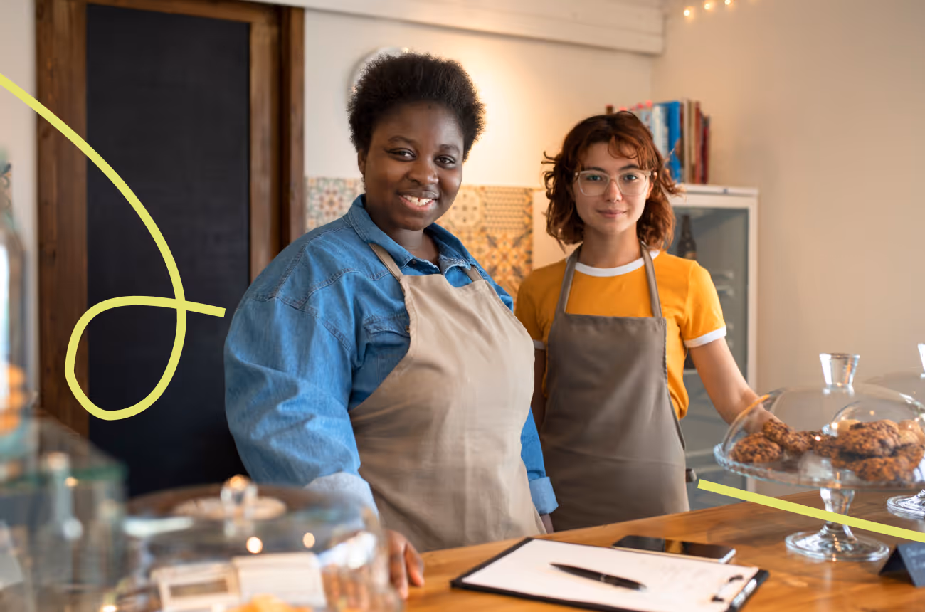 two cafe employees smiling at the camera, wearing aprons