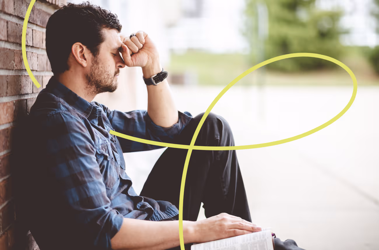 man sitting against a wall with hand on head looking stressed
