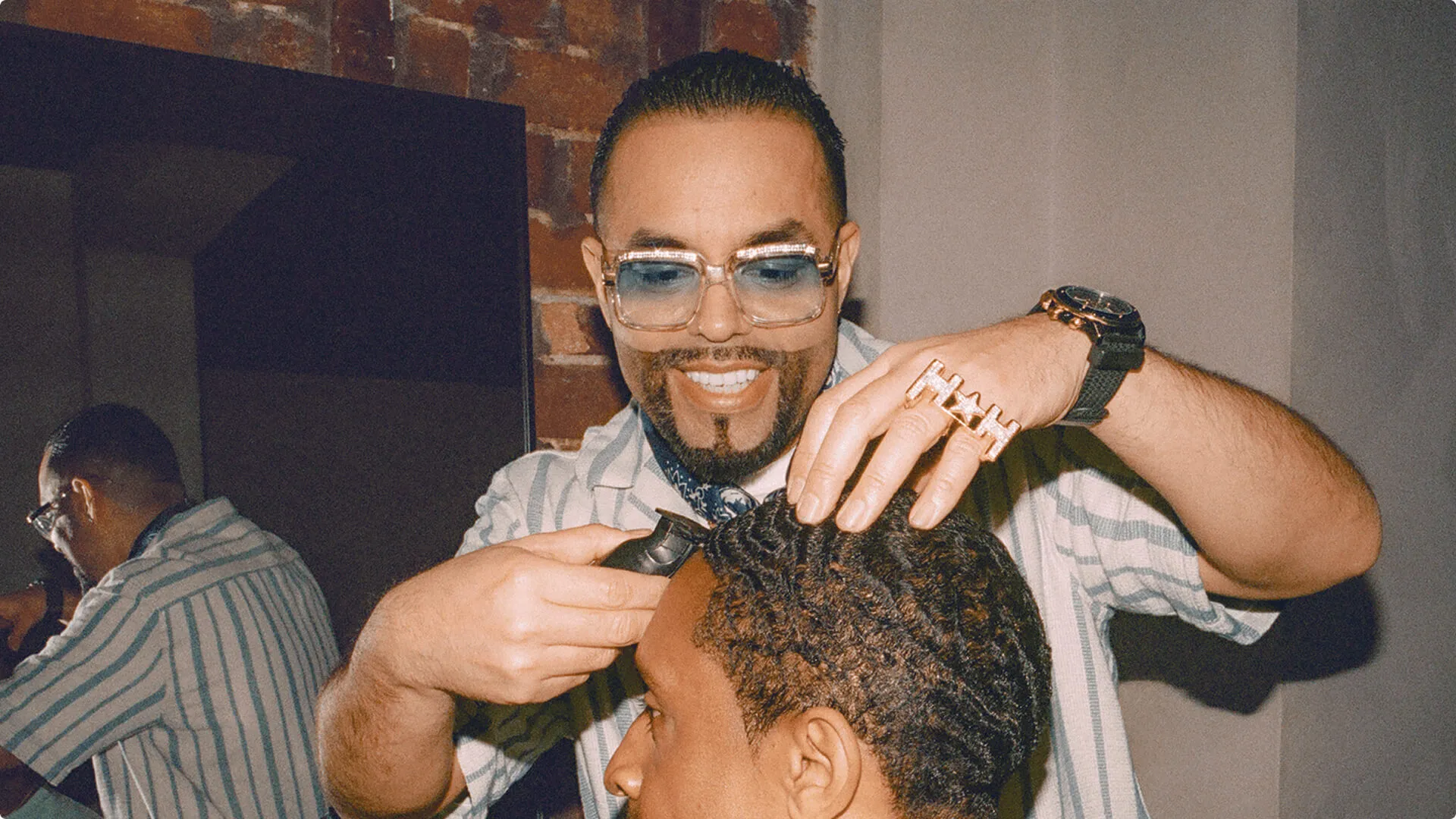 A barber smiling as he buzzes his male client’s hair